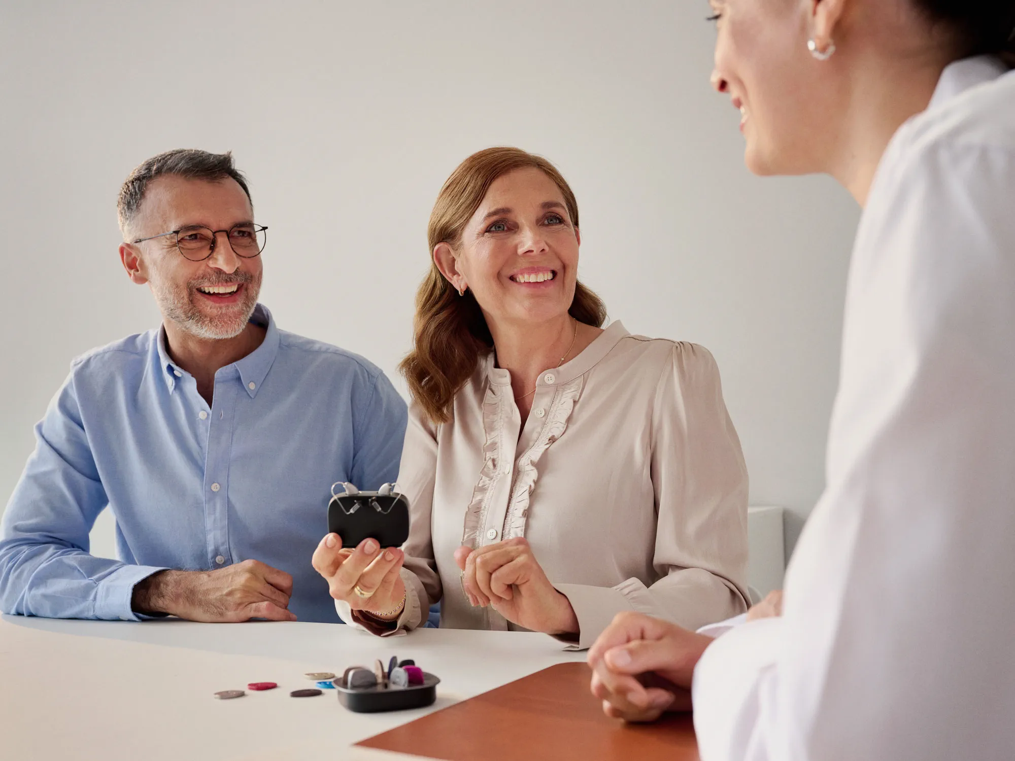 Cliente com perda auditiva a escolher entre aparelhos auditivos durante uma consulta com um especialista.