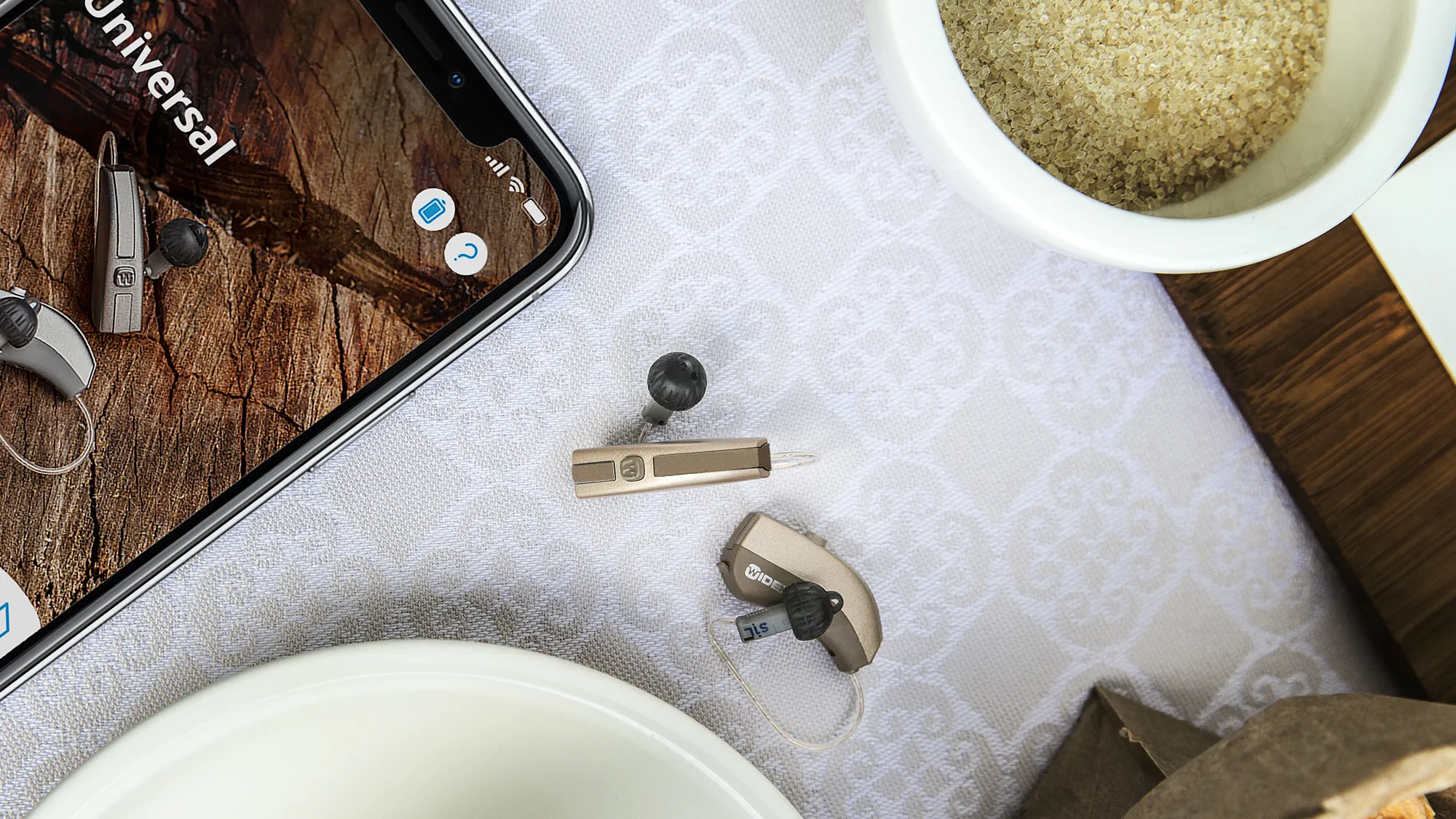 Aparelhos auditivos Widex Evoke mostrados sobre a mesa, comparados em tamanho com um smartphone.