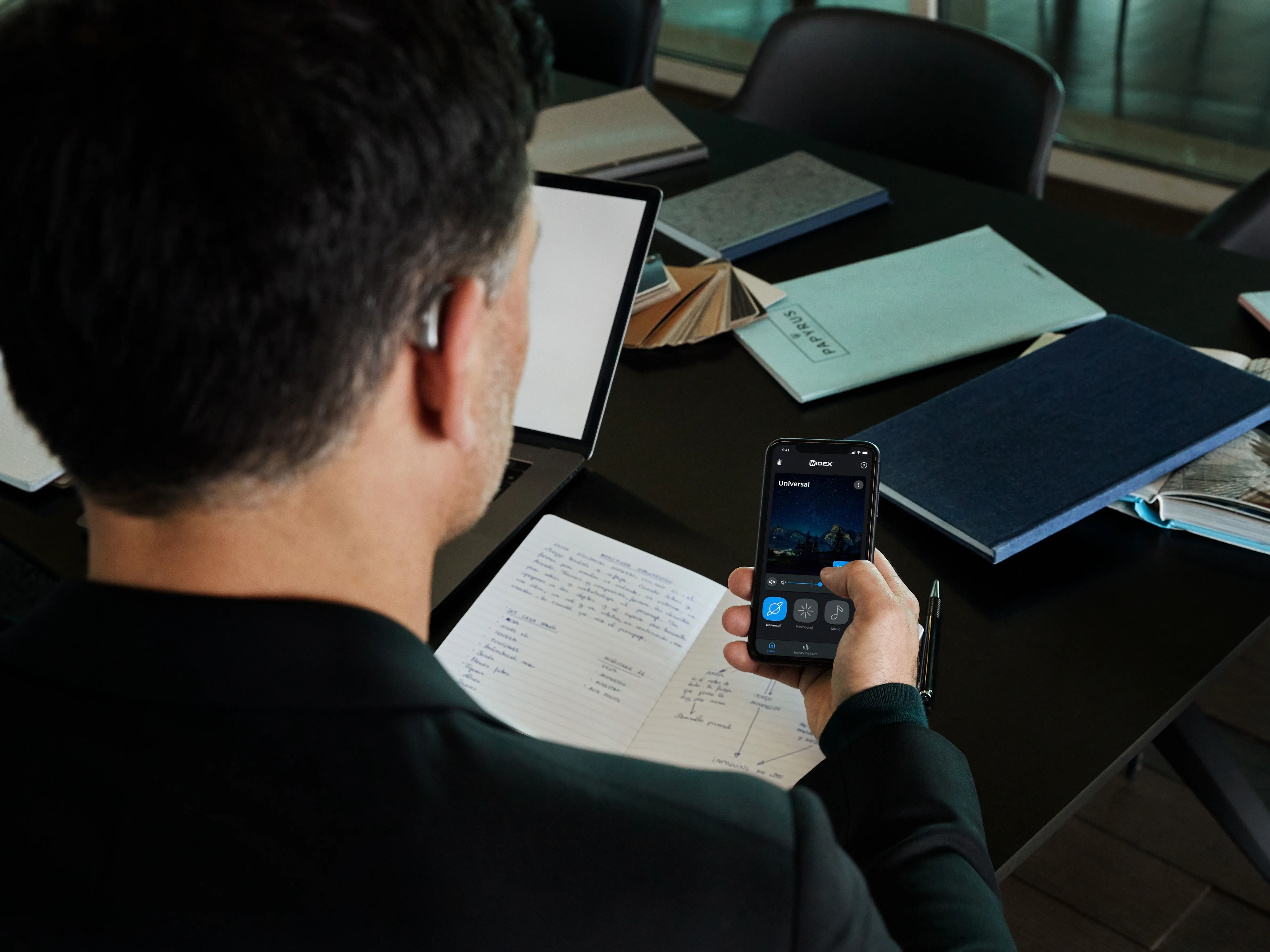 Homem a usar os aparelhos auditivos Widex Moment e a controlá-los através da aplicação Widex Moment no telemóvel.