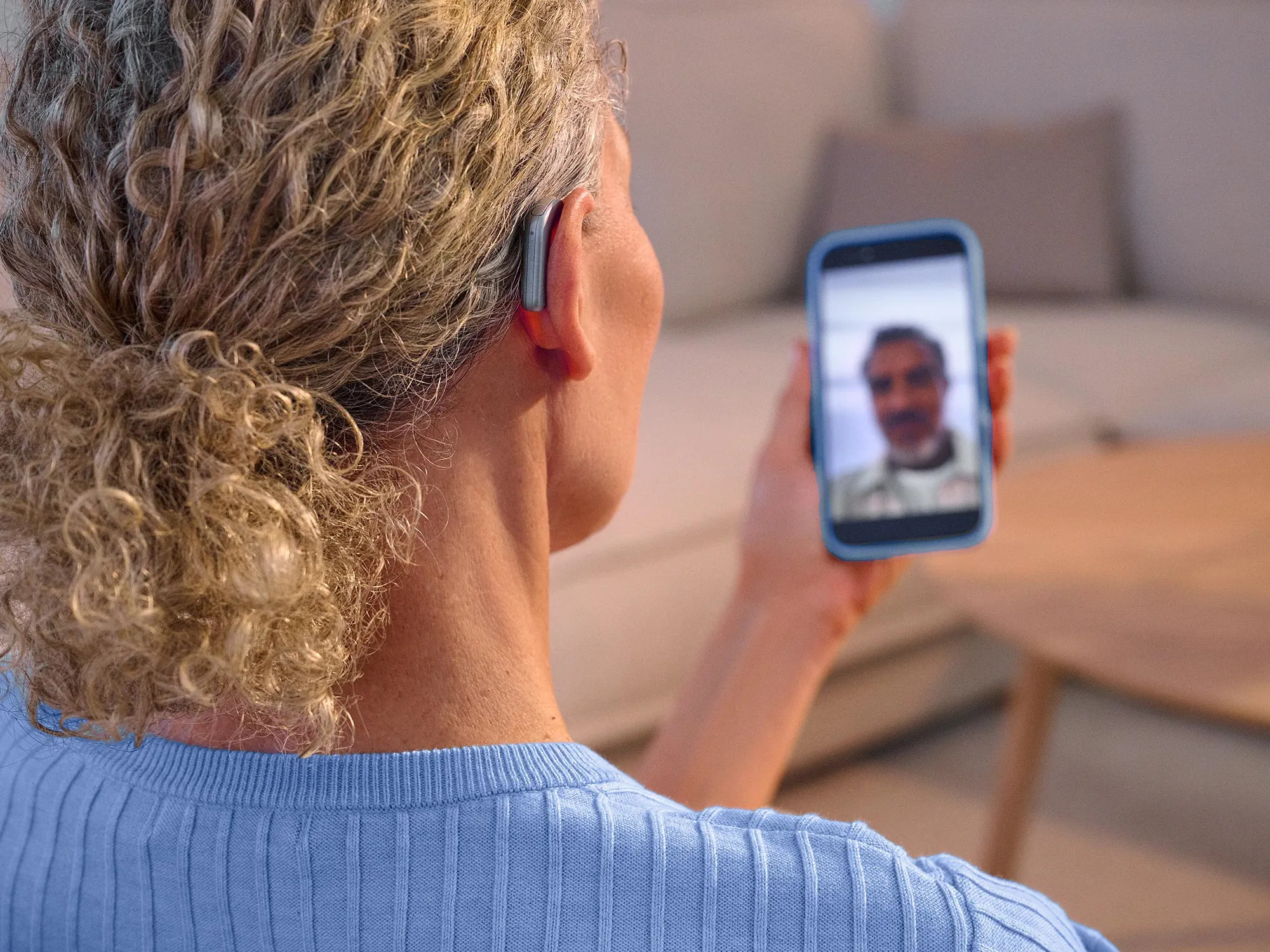 Mulher a fazer uma videochamada com uma amiga, usando aparelhos auditivos Widex Smart RIC e recebendo o som diretamente no aparelho auditivo.